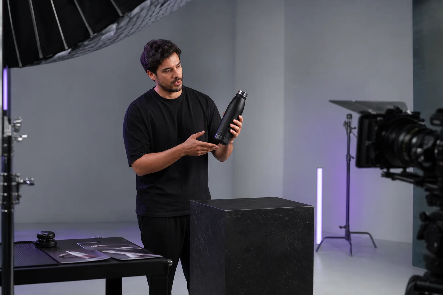 A black-clad creator demonstrating a matte-black bottle during a commercial studio shoot
